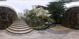 Outdoor HDR image featuring a curved staircase with railings, surrounded by greenery and urban backdrop for lighting scenes.