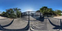 360-degree HDR panorama of a sunlit metal gate and cobblestone ground for realistic scene illumination.