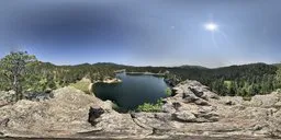 Panoramic HDR image of a serene lake surrounded by forested hills under a vibrant blue sky with soft clouds.