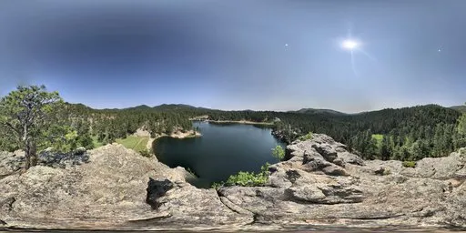 Panoramic HDR image of a serene lake surrounded by forested hills under a vibrant blue sky with soft clouds.