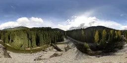 Aerial HDR panorama of a scenic river curving through a dense forest with a mountainous backdrop on a sunny day with clouds.