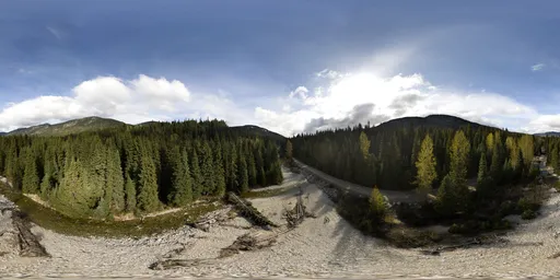 Aerial HDR panorama of a scenic river curving through a dense forest with a mountainous backdrop on a sunny day with clouds.
