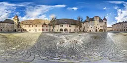 360-degree panoramic HDR image featuring cobblestone pavement and historic European buildings under a clear sky.