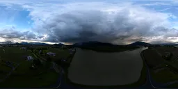 Aerial HDR panorama of sunset behind dark clouds over a serene Canadian landscape with lake and road.