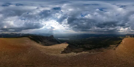Dynamic HDR showing sunlight piercing through storm clouds over a rugged mountain peak.