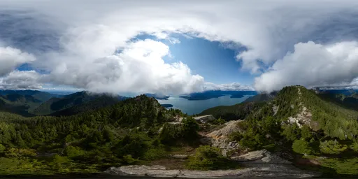 360-degree HDR panorama of a sunny mountain landscape with clouds over a coastal region.