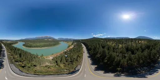 Aerial HDR image of a scenic highway winding by a turquoise river amidst lush Canadian forests with mountains in the background.