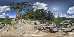 360-degree HDR panorama of a rocky hillside with trees under a blue sky with white clouds.