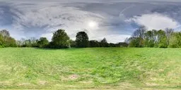 Panoramic HDR of serene springtime field with green grass, leafless trees, and clear blue sky with sparse clouds.