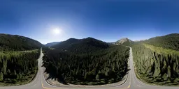 360-degree HDR panorama of a sunlit mountainous landscape with a winding road and dense forests for realistic scene lighting.