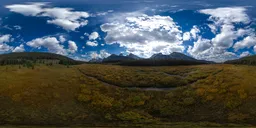 Panoramic HDR image of a verdant valley with surrounding mountains under a dynamic cloudy sky.
