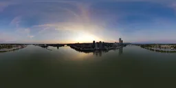 Panoramic evening skyline with a vibrant sunset behind skyscrapers, reflecting in a calm river.