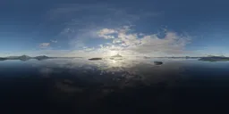Dynamic aerial HDR panorama featuring sunlit clouds over a serene mountainous region with reflective waters.