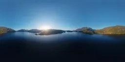 360-degree high-resolution aerial HDR panorama featuring tranquil lake water reflecting a serene sunset amidst the mountainous terrain.