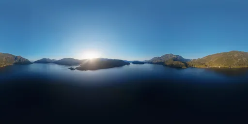 360-degree high-resolution aerial HDR panorama featuring tranquil lake water reflecting a serene sunset amidst the mountainous terrain.