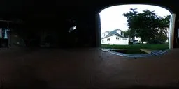 360-degree HDR panorama from a garage opening to a house with a surrounding lush landscape.