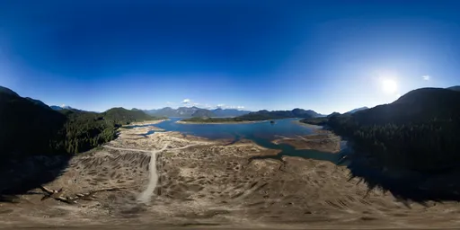 High-resolution HDR image featuring a sunlit aerial view with clear blue skies over an expansive lake, surrounded by mountainous terrain.