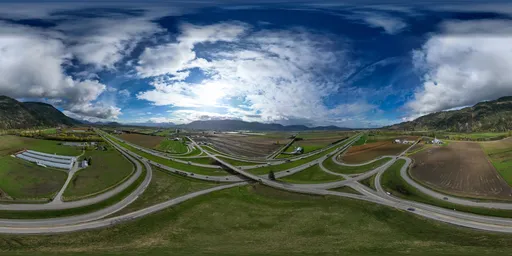 360 HDR panoramic image of a scenic valley and highway intersection with cloudy skies and distant mountains.