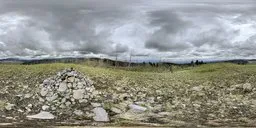 Overcast sky HDR panorama with lush green grass and stone pile, ideal for realistic environmental lighting.