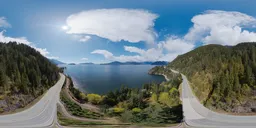 Aerial HDR panorama of ocean coast with mountainous landscape, sunny sky and fluffy clouds in BC, Canada.
