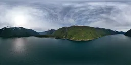 360-degree HDR panorama of a serene lake with surrounding mountains under a dynamic sky.