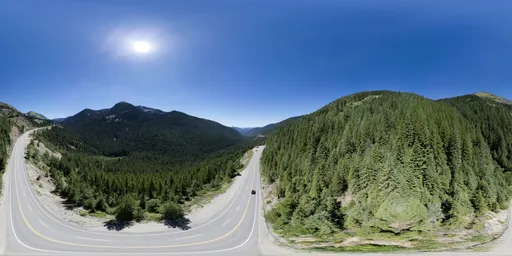 Aerial HDR panorama of scenic highway cutting through lush green mountainous landscape on a clear day.