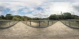 360-degree HDR panorama of a concrete bridge with glass balustrade overlooking an artificial lake surrounded by greenery on a cloudy day.