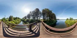 360-degree HDR of tranquil wooden bridge over calm water with trees and clear blue sky for realistic scene lighting.